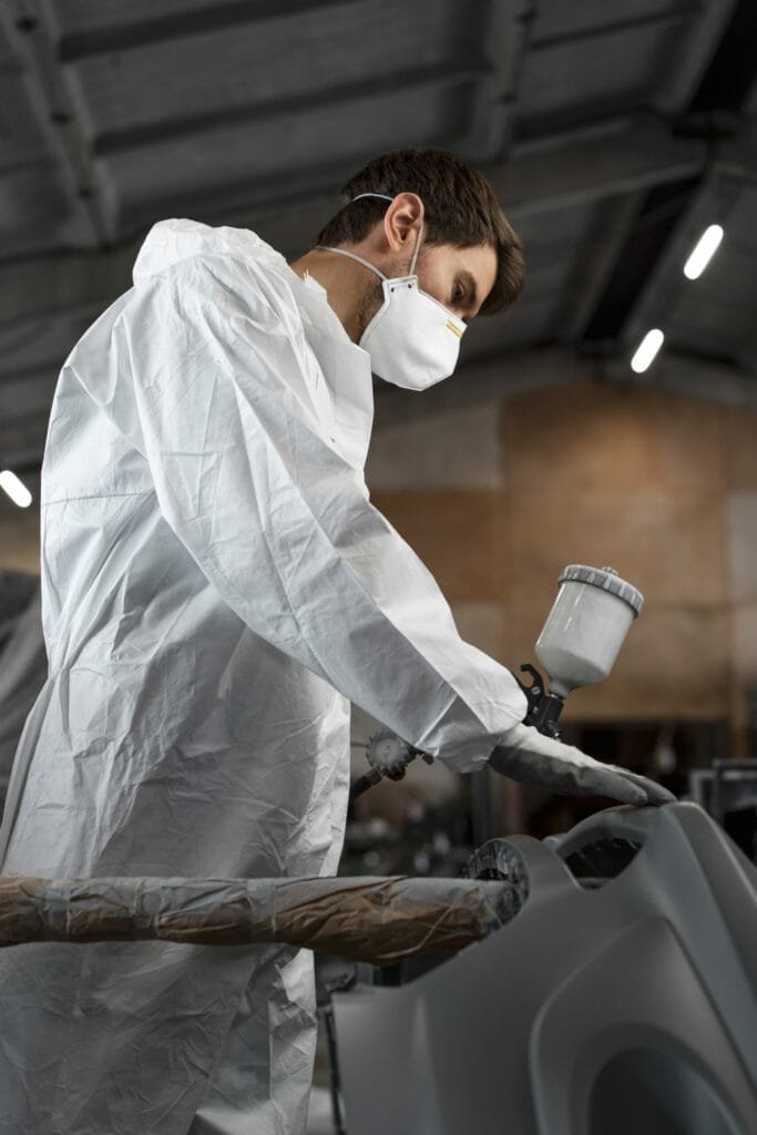 A man wearing a mask and white suit in an auto body shop.